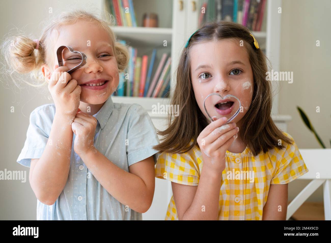 Verspielte Mädchen mit herzförmigem Keksschneider zu Hause Stockfoto