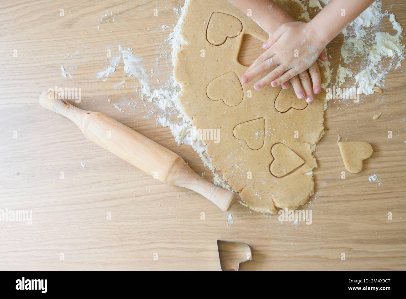 Hände von Mädchen, die Keksteig schneiden, mit Schneidevorrichtung auf dem Tisch zu Hause Stockfoto