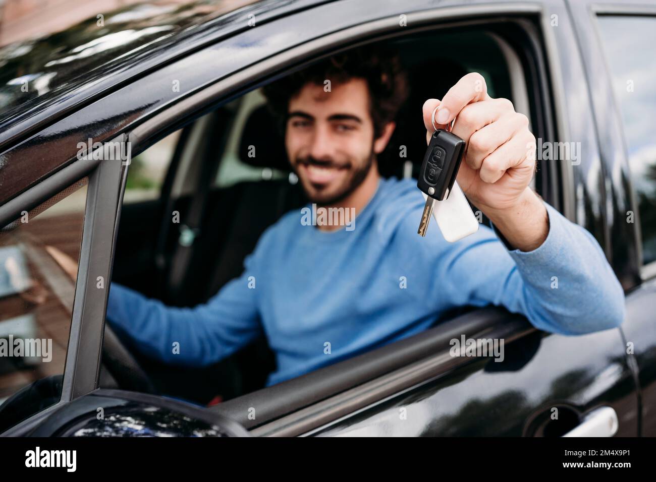Ein junger Mann, der im Auto sitzt und den Schlüssel zeigt Stockfoto