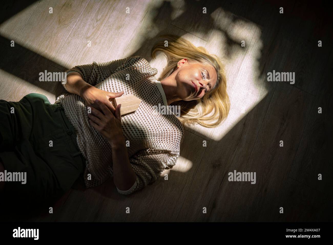 Reife Frau hält Hausmodell-Objekt mit Sonnenlicht im Gesicht Stockfoto