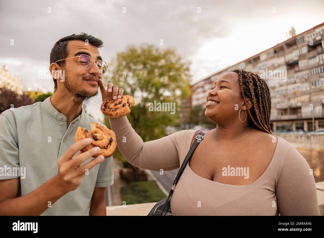 Eine glückliche junge Frau, die ihrem Freund das Gesicht abwischt und mit Süßigkeiten unter dem wolkigen Himmel steht Stockfoto