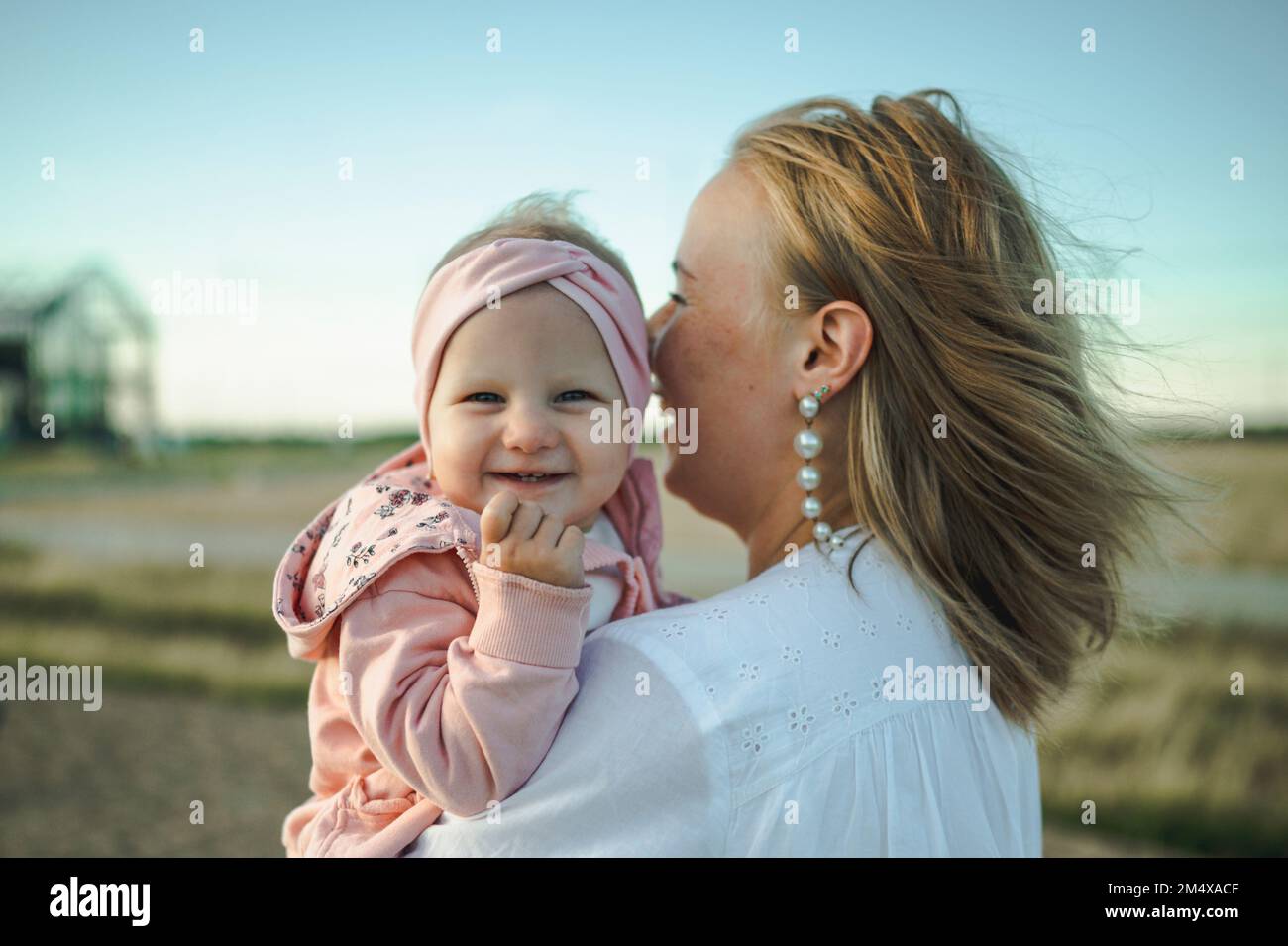 Fröhliches süßes Mädchen mit Mutter, die vor dem Himmel steht Stockfoto