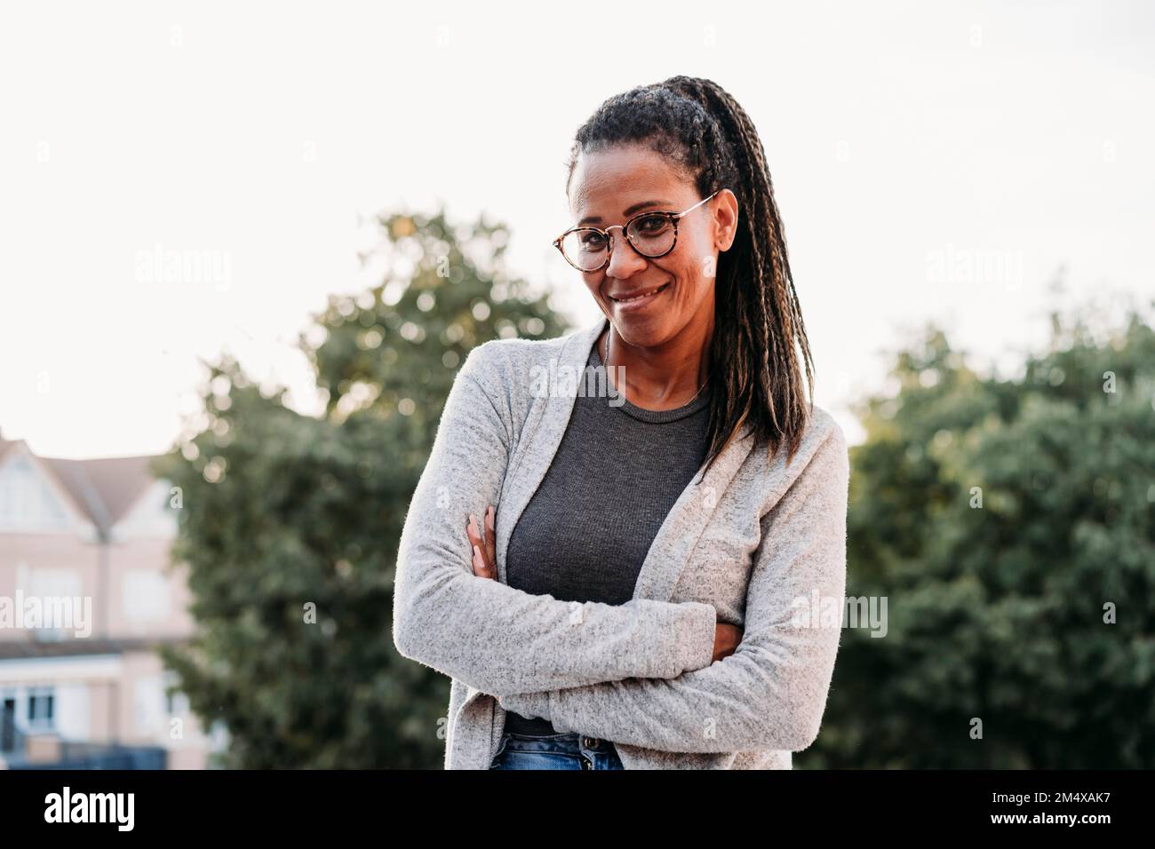 Glückliche Frau mit verschränkten Armen bei Sonnenuntergang Stockfoto