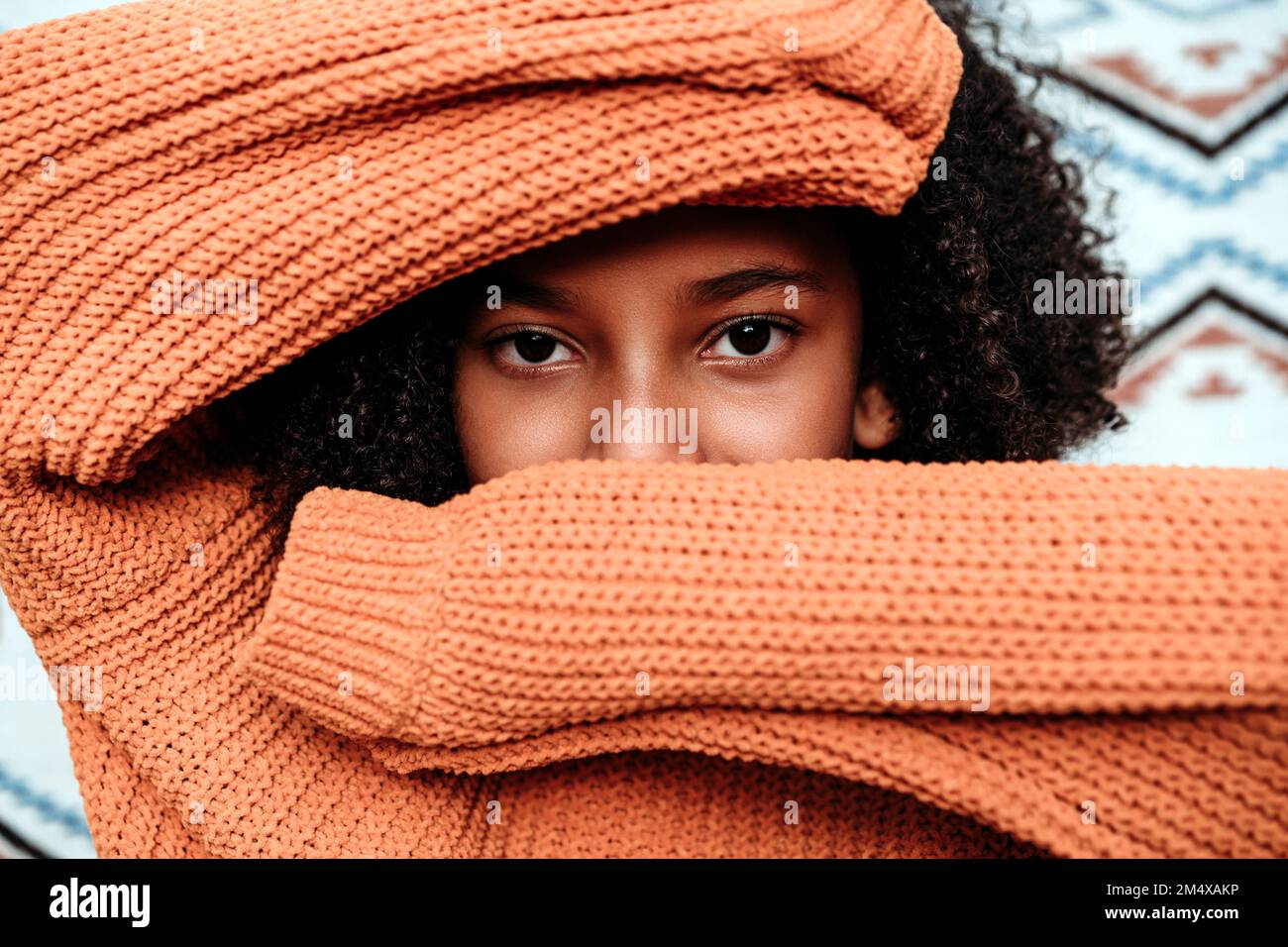 Ein Mädchen mit orangefarbenem Pullover, das das Gesicht bedeckt Stockfoto