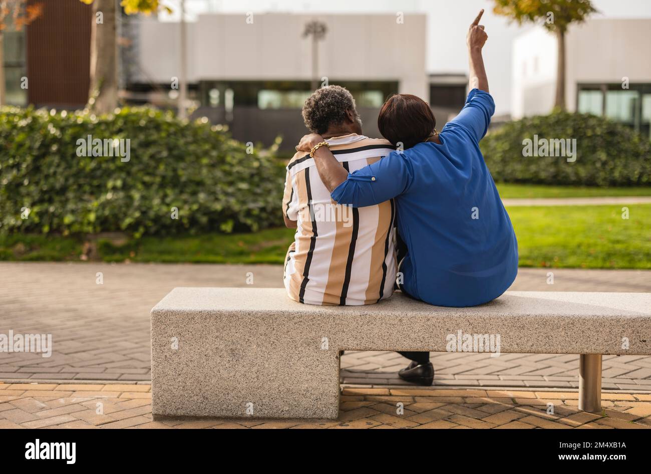 Eine Frau, die mit dem Arm um den Mann sitzt, auf einer Bank im Park Stockfoto