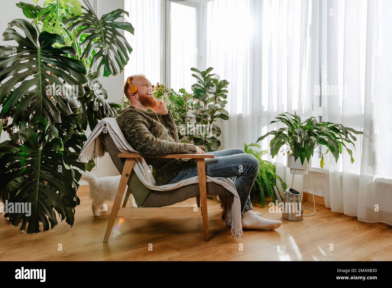 Ein Mann mit Kopfhörern, der zu Hause auf einem Stuhl sitzt Stockfoto