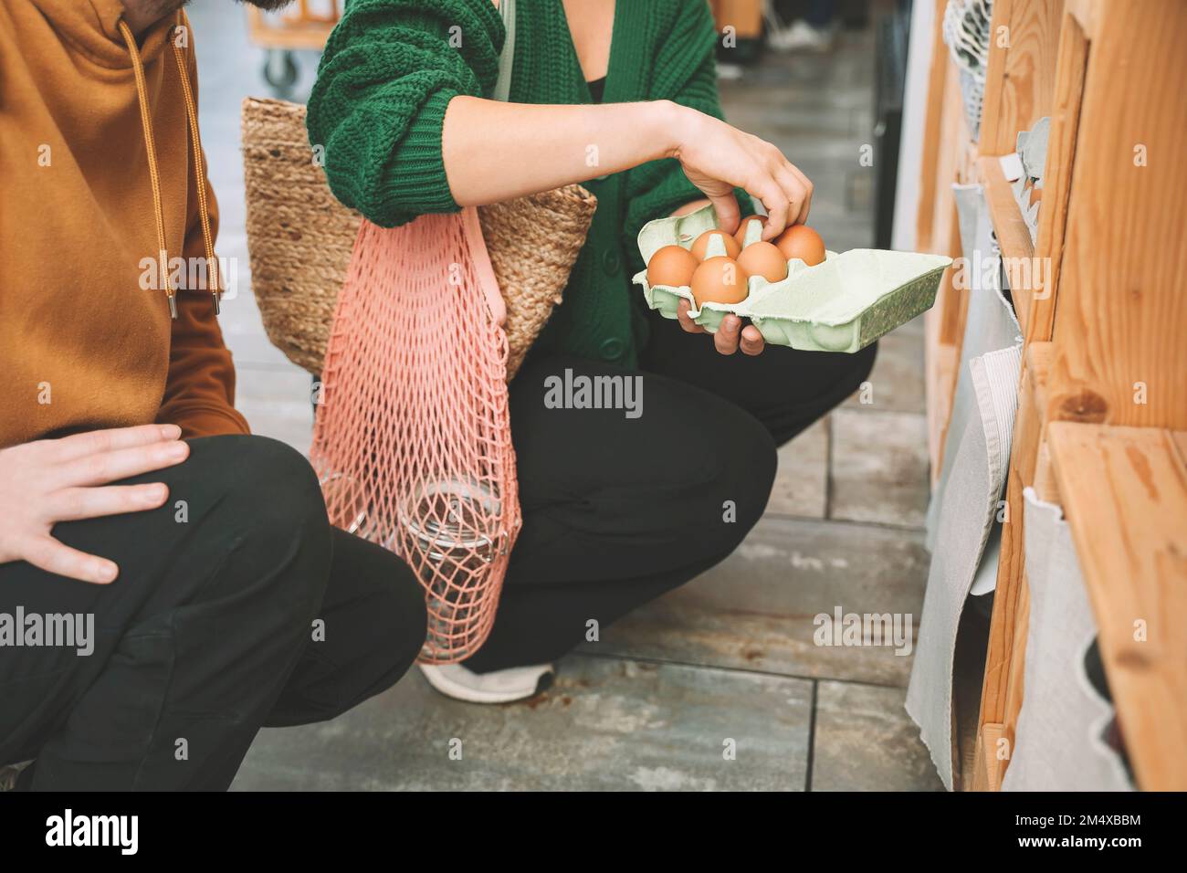 Eine Frau, die Eier in Kartons untersucht, von einem Mann im Laden Stockfoto