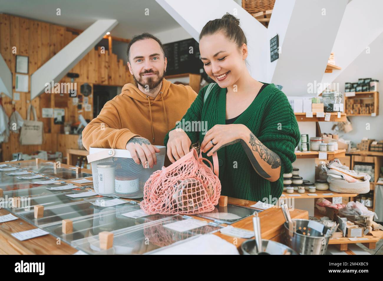 Lächelnde Frau mit Netztasche von Mann an der Theke im Supermarkt Stockfoto
