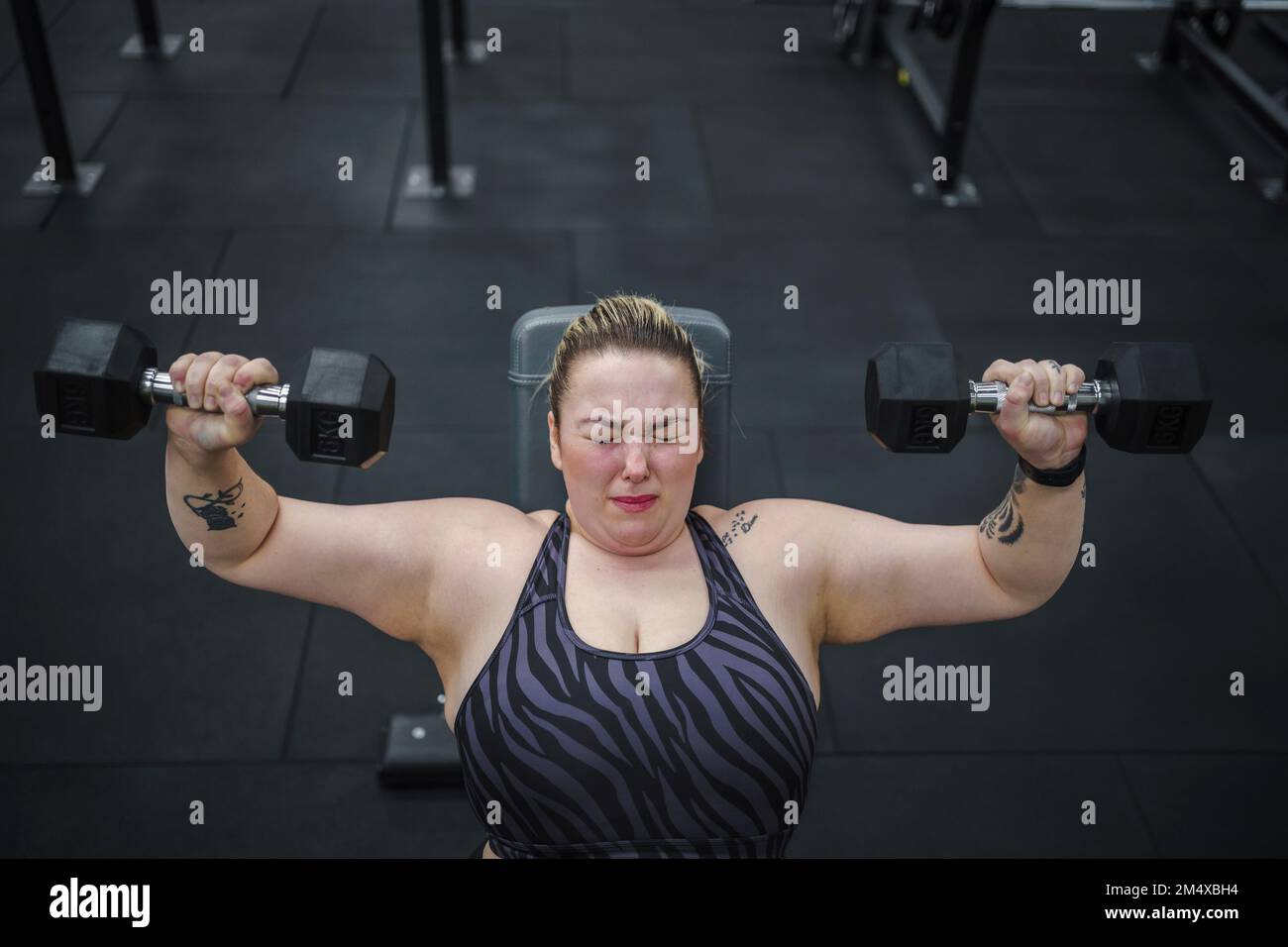 Engagierte übergewichtige Frau, die im Fitnessstudio mit Kurzhanteln trainiert Stockfoto