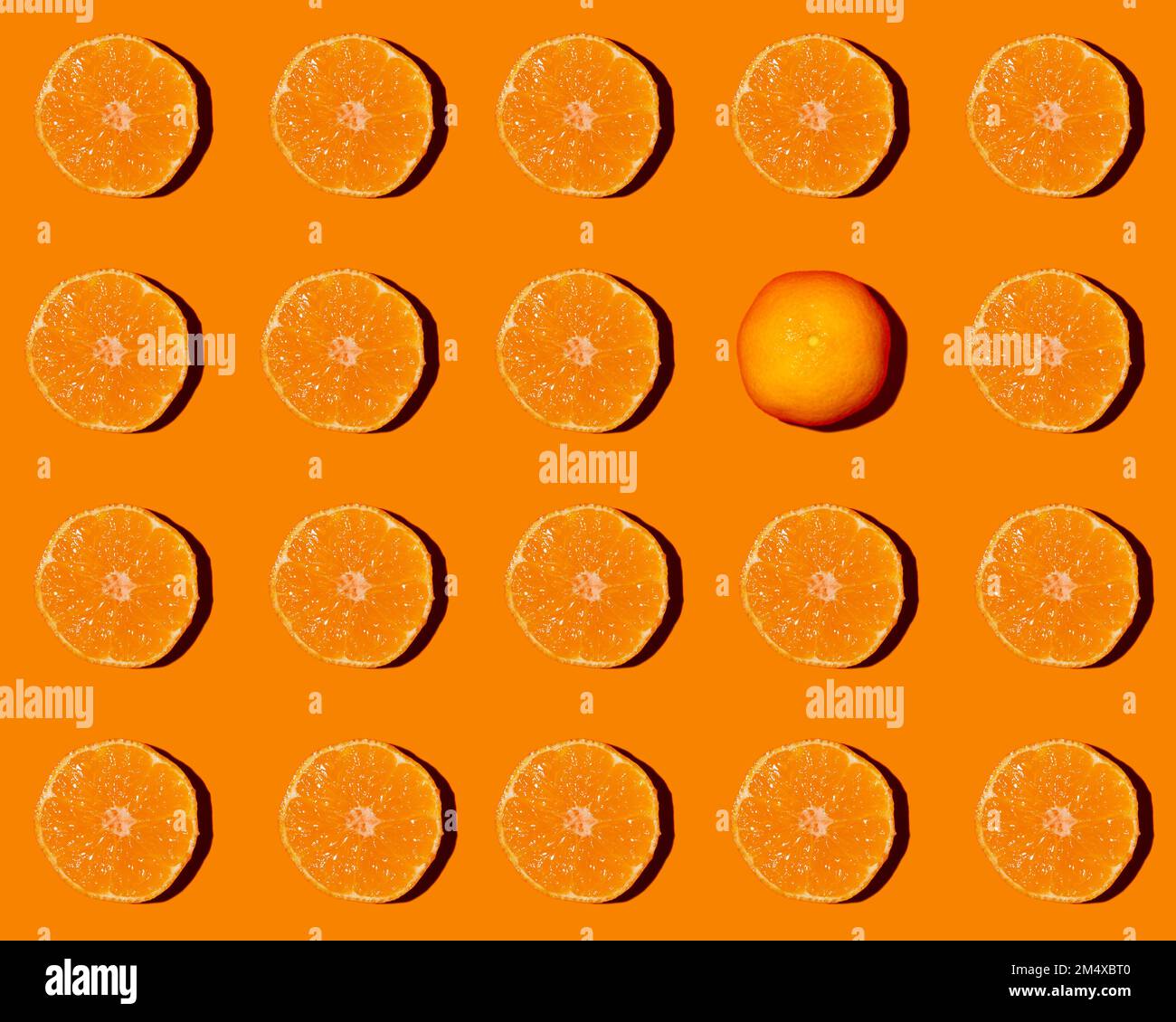Muster aus halbierten Tangerinen, flach auf orangefarbenem Hintergrund gelegt, wobei eine einzelne davon verkehrt herum liegt Stockfoto