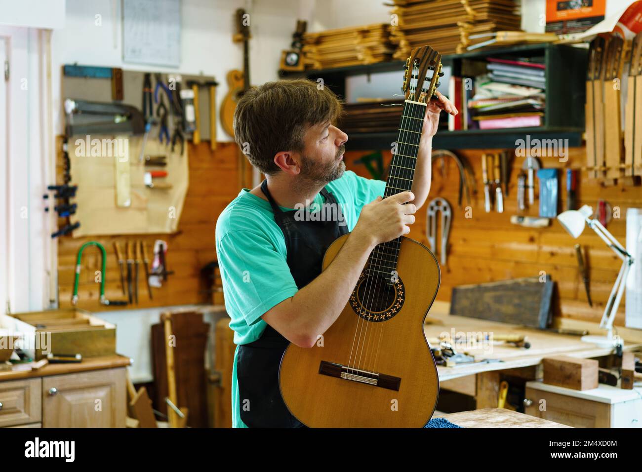 Reifer Handwerker, der Gitarrenstränge in der Werkstatt justiert Stockfoto