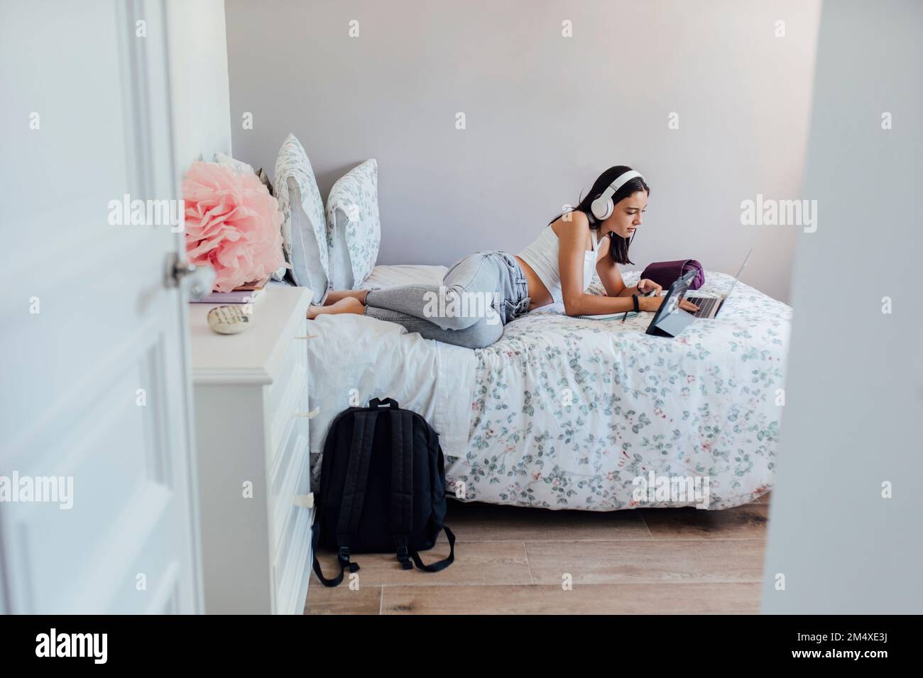 Mädchen mit Kopfhörern, die zu Hause mit kabellosen Technologien auf dem Bett liegt Stockfoto