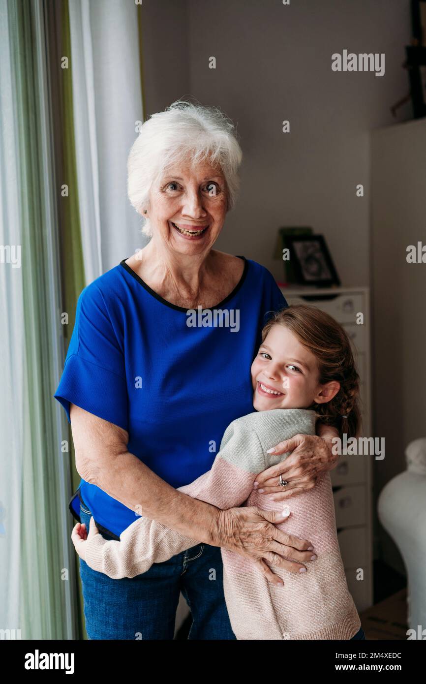 Glückliches Mädchen, das Großmutter zu Hause umarmt Stockfoto