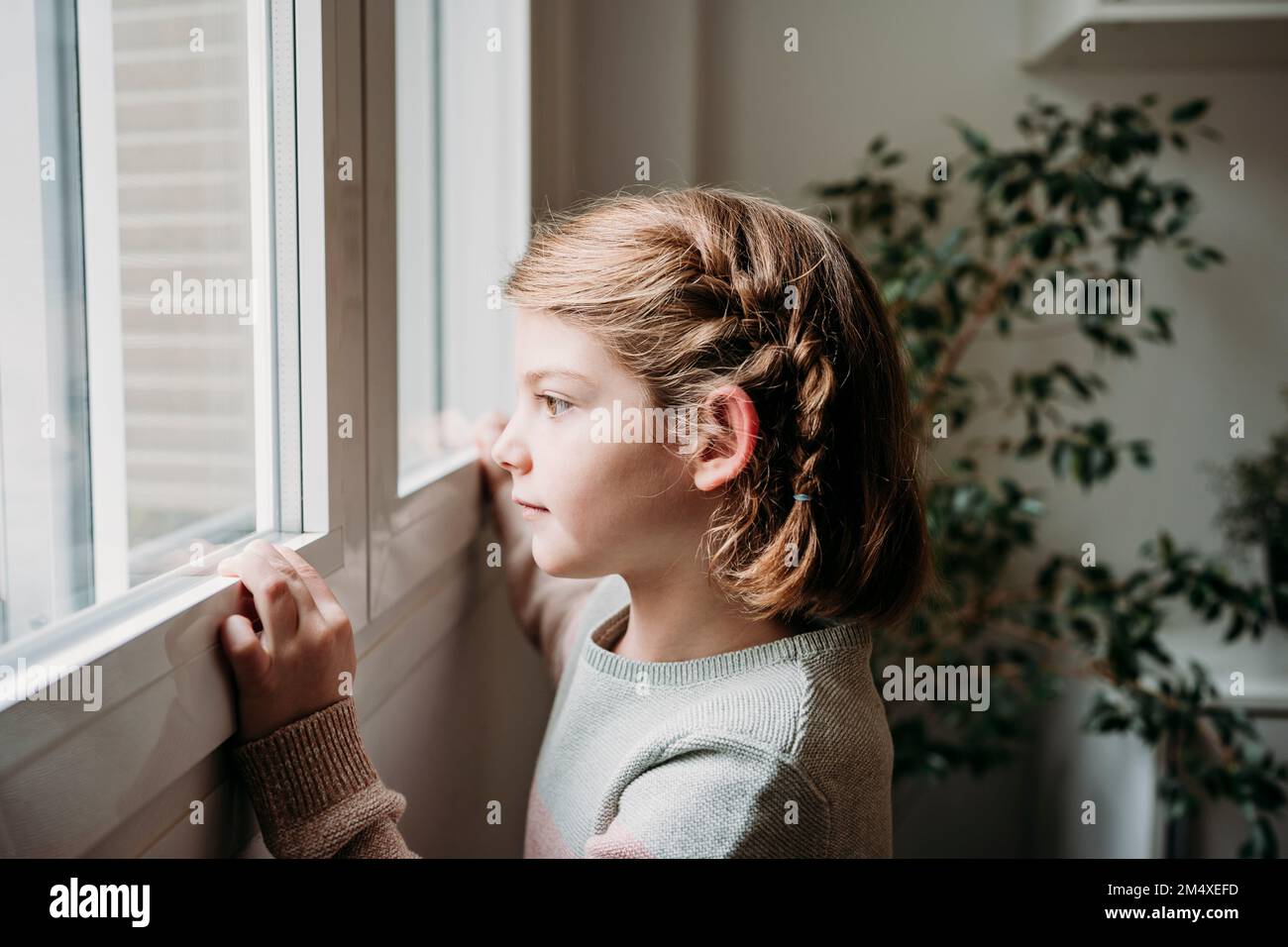 Ein rücksichtsvolles Mädchen, das zu Hause durch das Fenster schaut Stockfoto