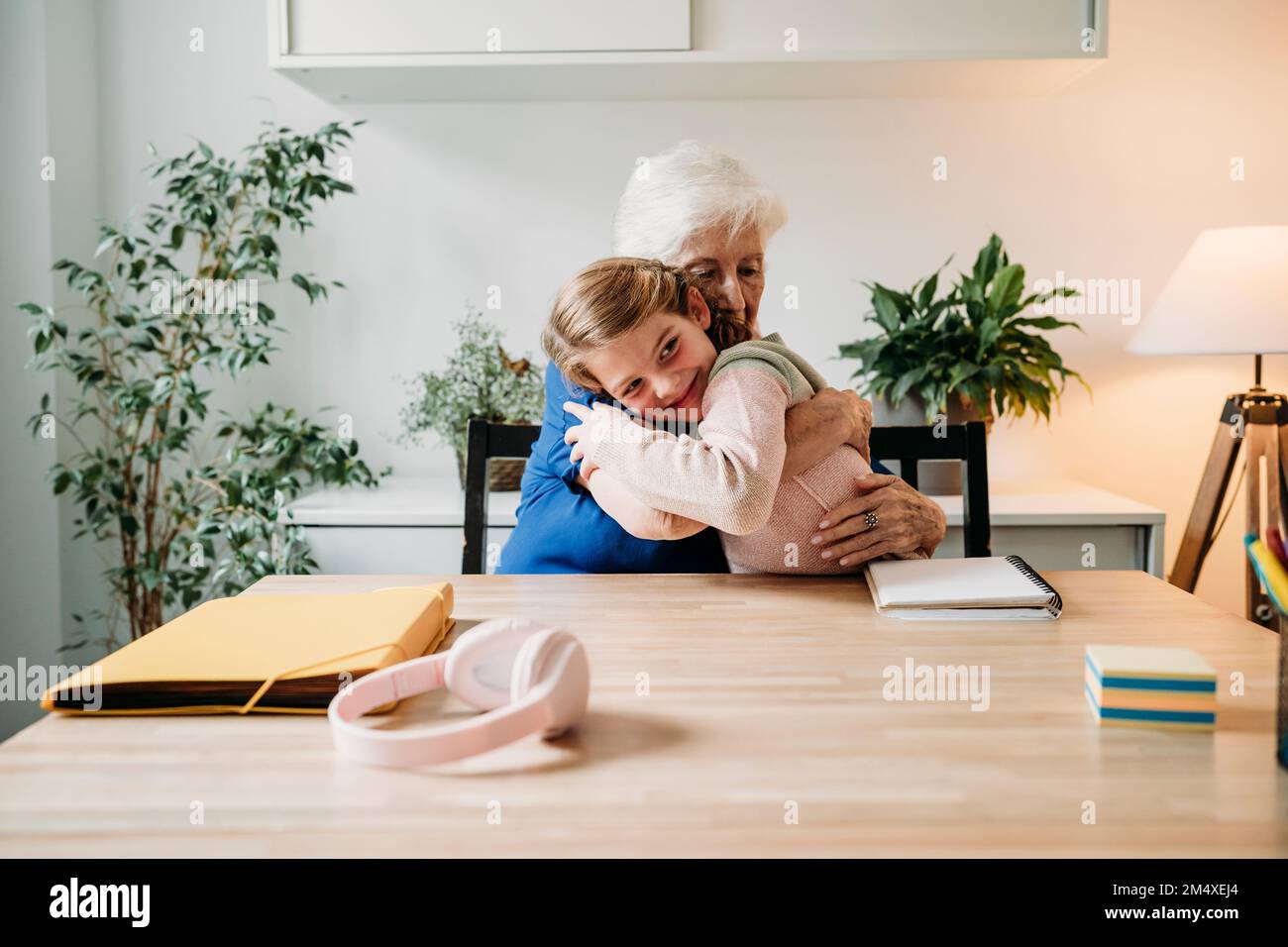 Glückliches Mädchen, das Großmutter zu Hause umarmt Stockfoto