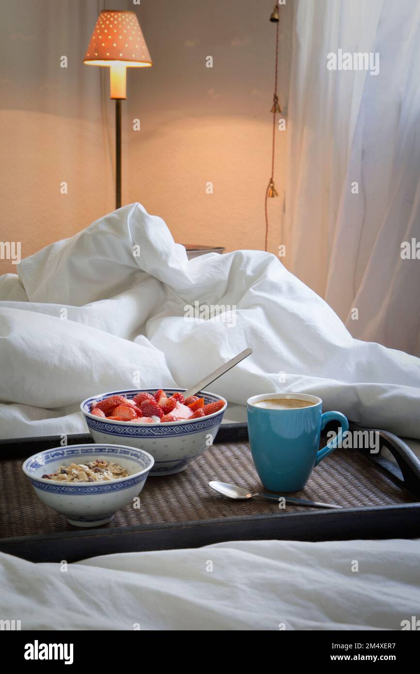 Tablett mit einer Tasse Kaffee, Müsli und Joghurt mit Erdbeeren auf dem Bett Stockfoto