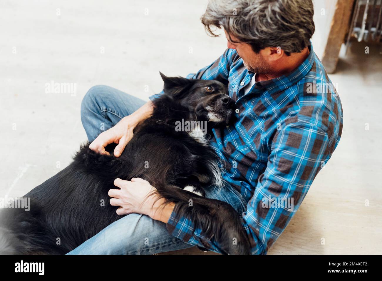 Handwerker, der in der Werkstatt mit dem Hund spielt Stockfoto