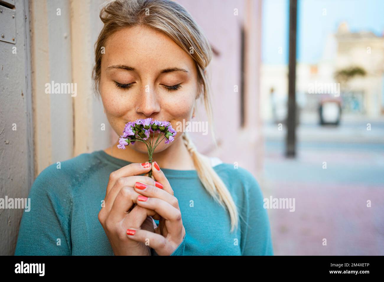 Schöne Frau mit geschlossenen Augen, die kleine Blumen auf dem Fußweg riecht Stockfoto