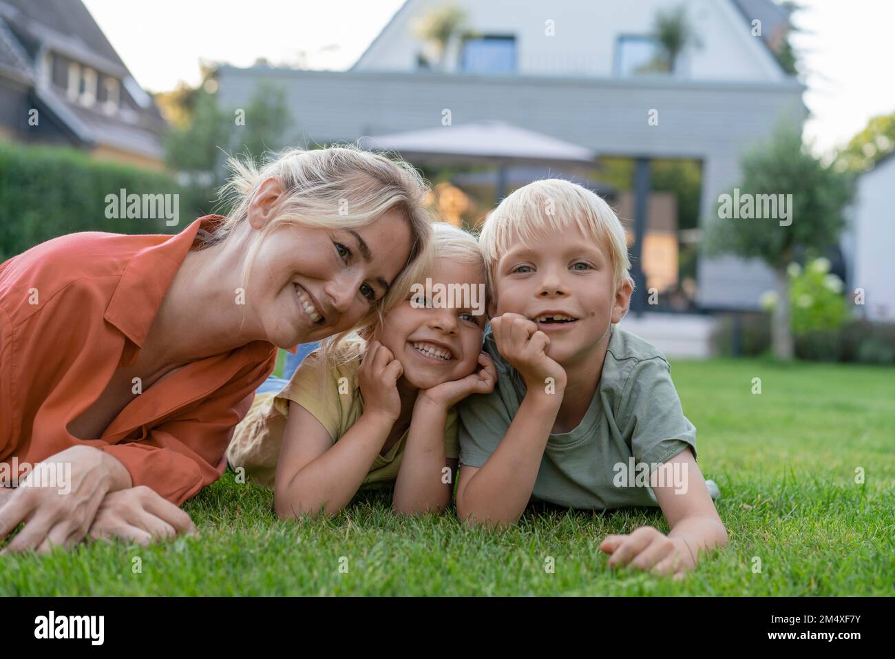 Glückliche Mutter mit Kindern, die sich im Garten auf Ellbogen lehnen Stockfoto