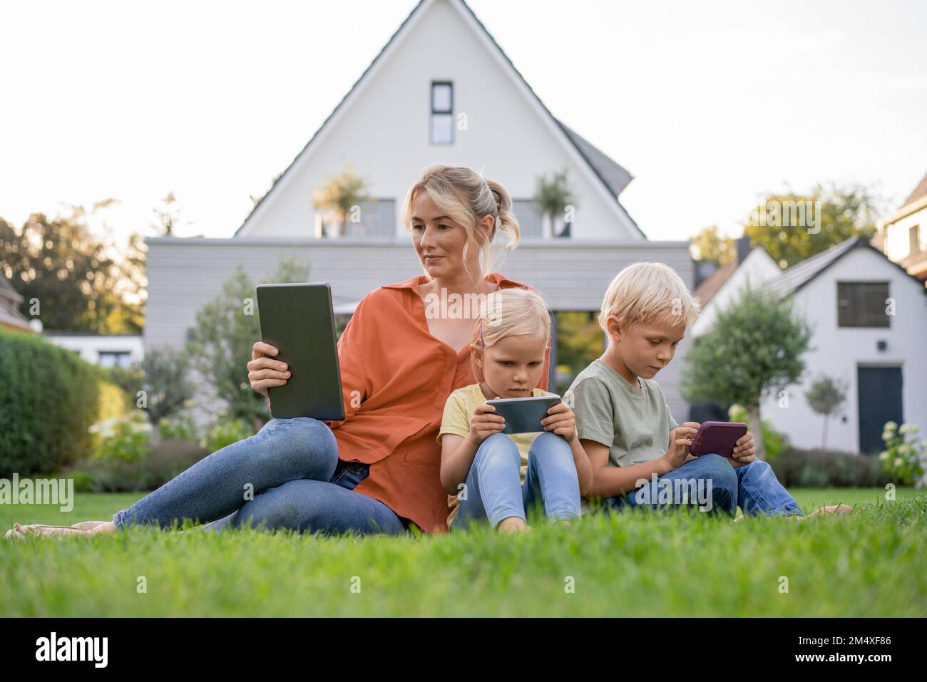 Familie mit kabelloser Technologie, die auf dem Rasen im Garten sitzt Stockfoto