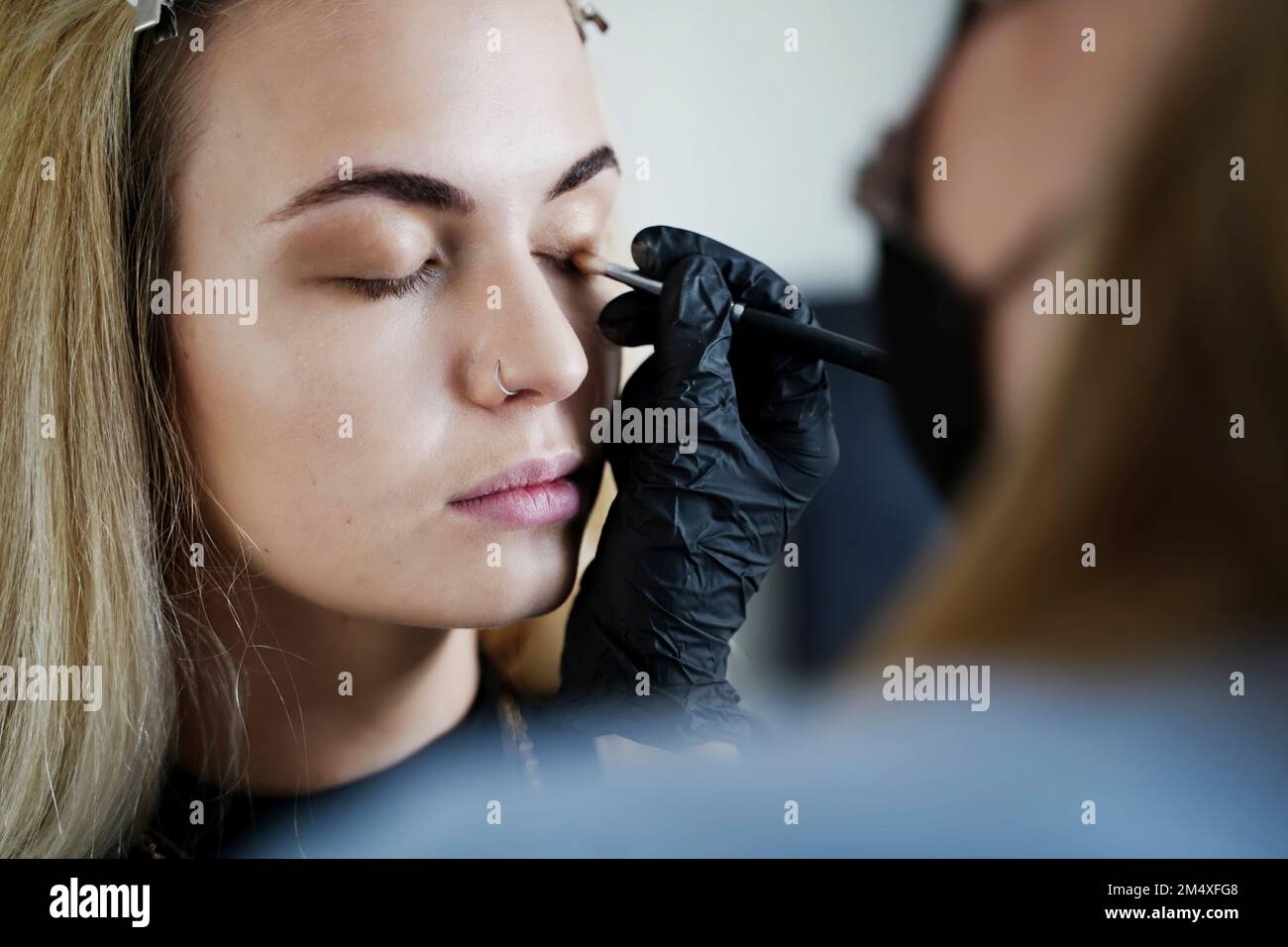 Make-up-Künstler, der im Salon Augenschatten auf das Lid des Kunden aufträgt Stockfoto