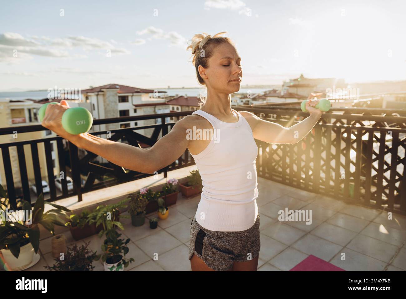 Eine Frau, die bei Sonnenuntergang auf der Dachterrasse Übungen mit Kurzhanteln macht Stockfoto