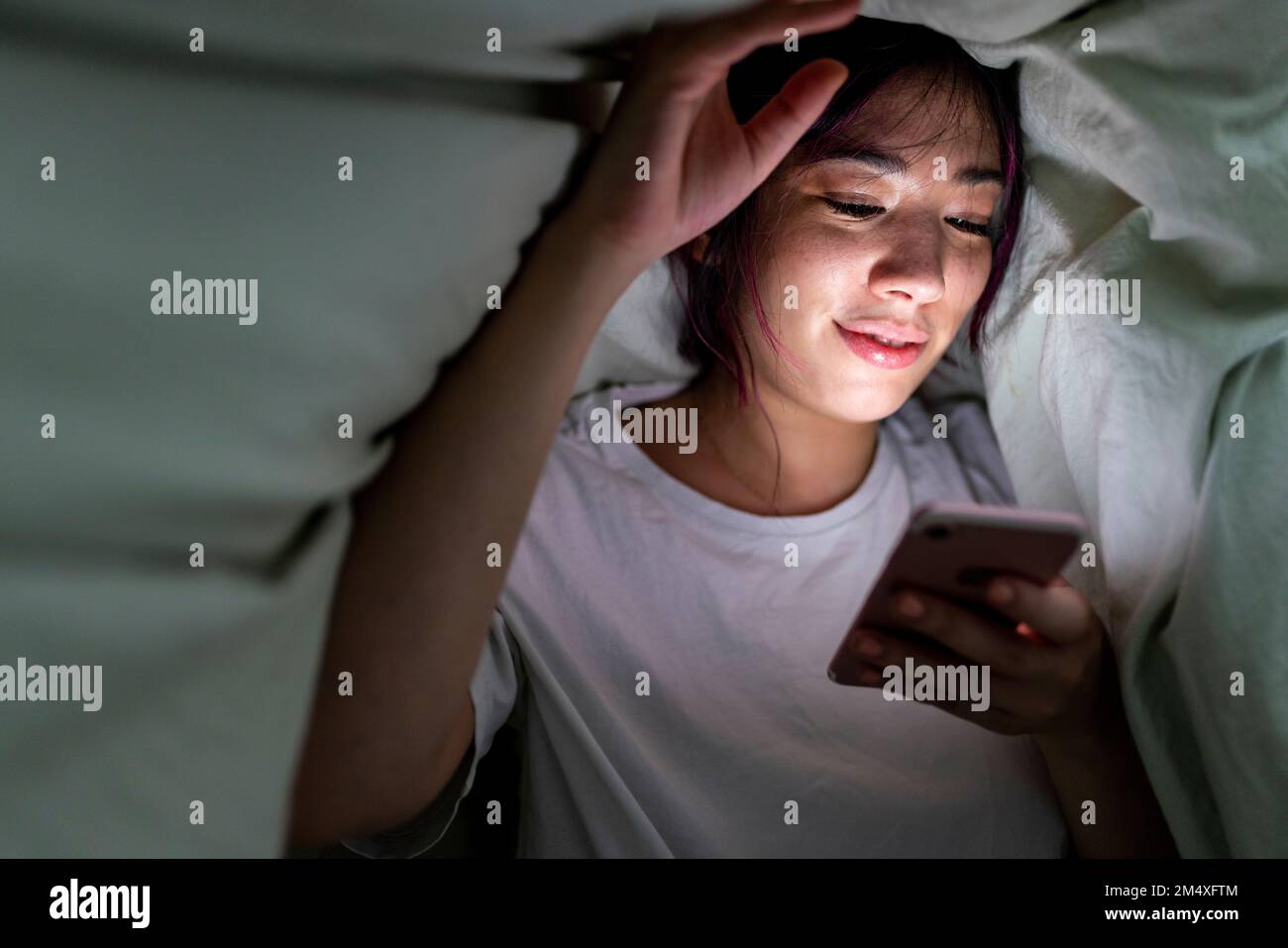 Lächelnde Frau, die zu Hause ein Smartphone unter der Decke benutzt Stockfoto