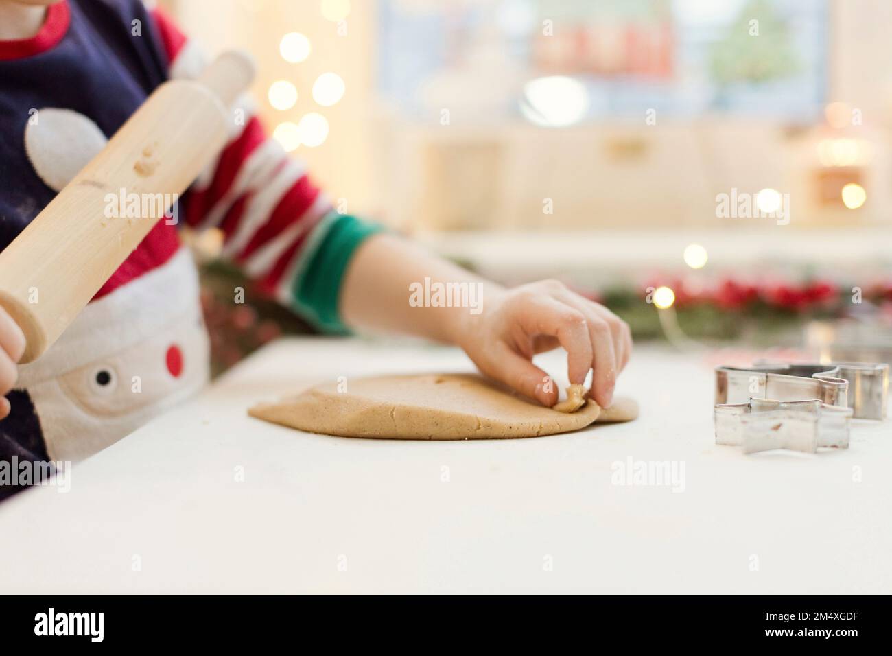 Die Hand eines Jungen, der Lebkuchenteig am Küchentisch rollt Stockfoto