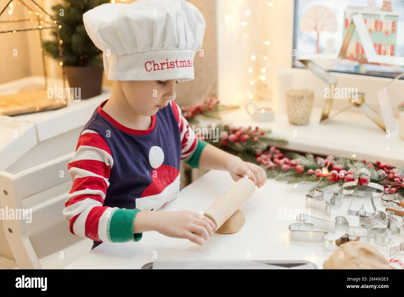 Ein Junge, der den Hut des Küchenchefs trägt und Lebkuchenteig an der Küchentheke rollt Stockfoto