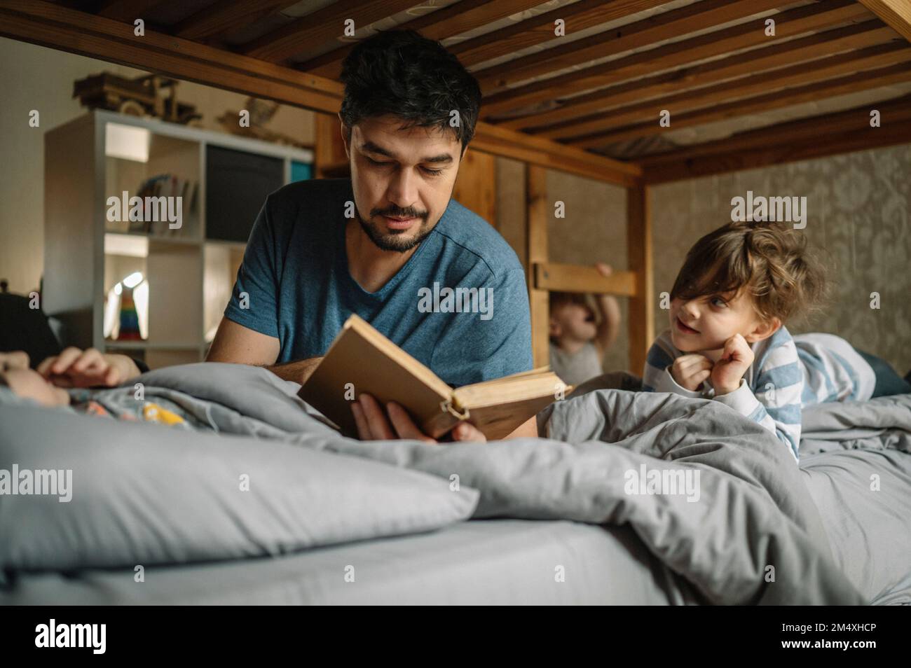 Vater liest seinen Söhnen zu Hause im Bett ein Buch vor Stockfoto