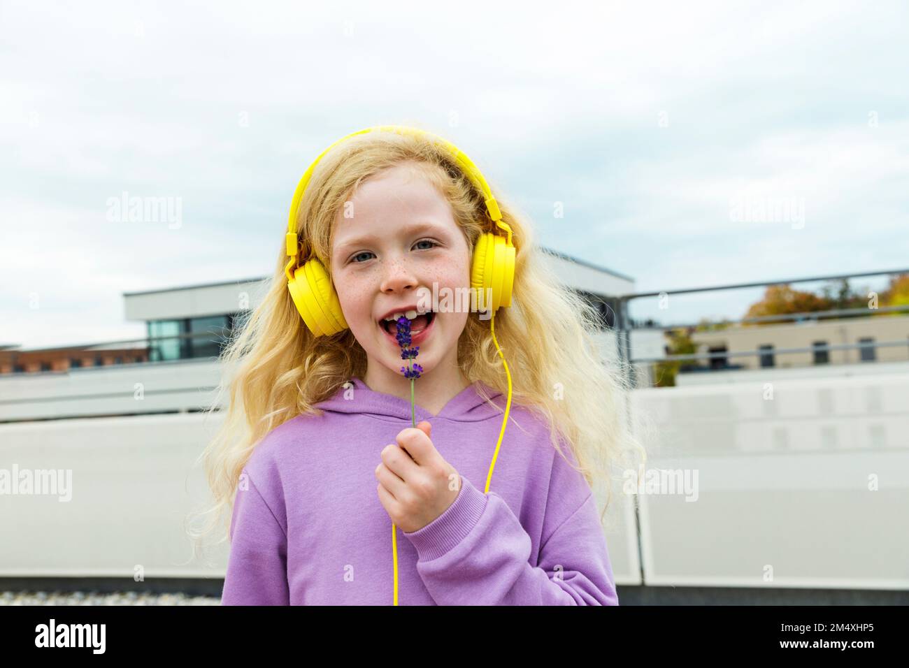 Glückliches Mädchen mit kleinen Blumen, das Musik über Kopfhörer auf der Terrasse hört Stockfoto