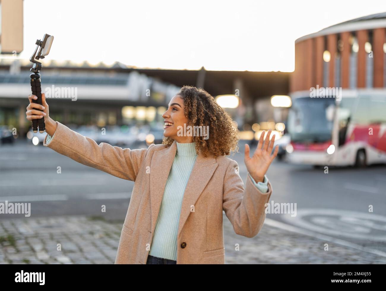 Lächelnde Frau mit Gesten und Videoaufzeichnung über Mobiltelefon auf Stativ Stockfoto