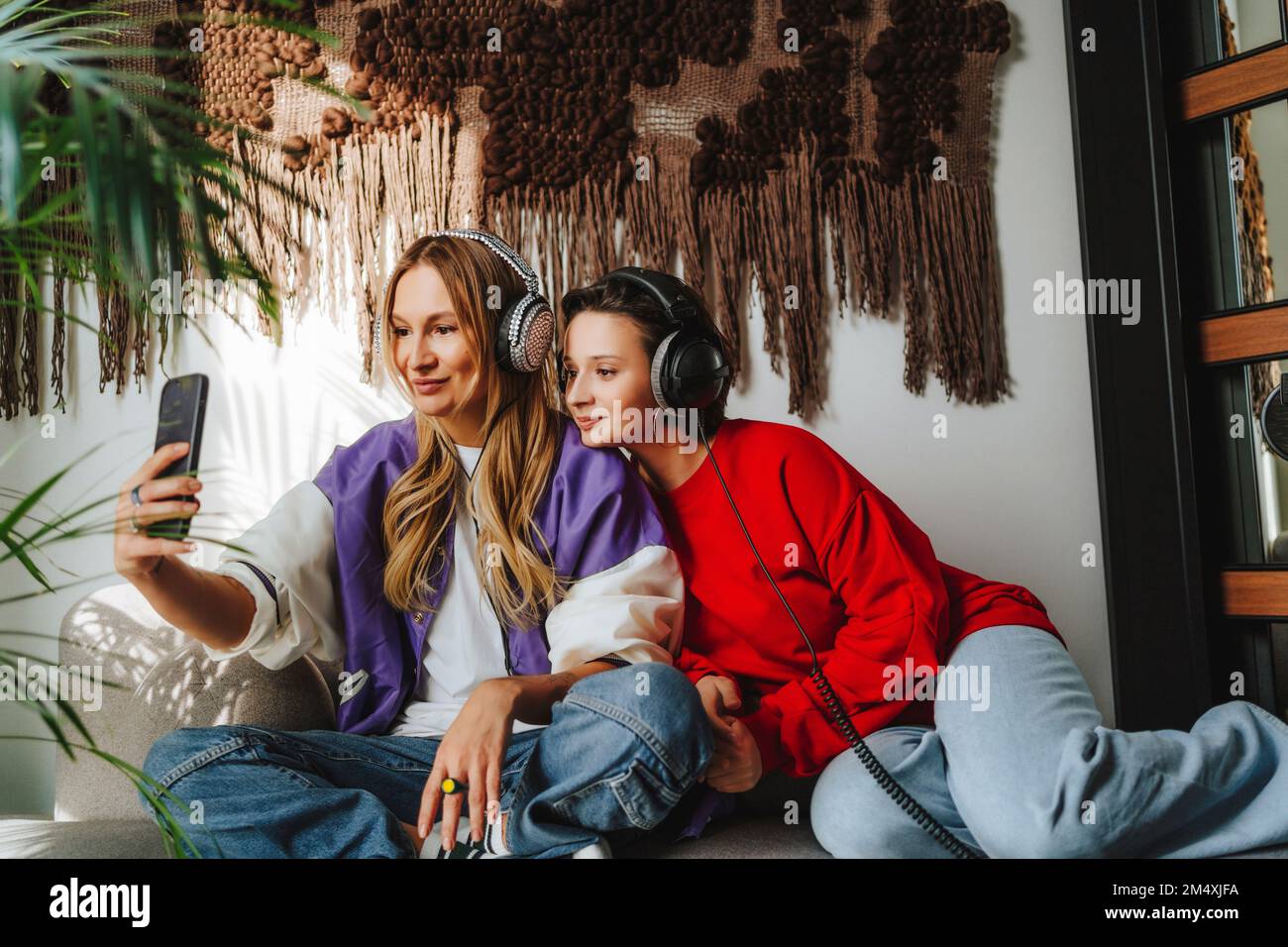 Lächelnder Musiker mit einem Kollegen, der Selfie per Mobiltelefon auf dem Sofa im Studio macht Stockfoto