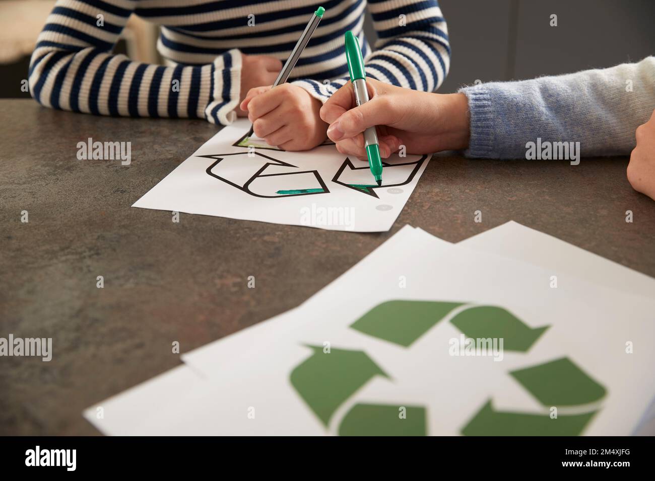 Hände von Mädchen, die ein Recycling-Symbol mit Stift am Tisch malen Stockfoto