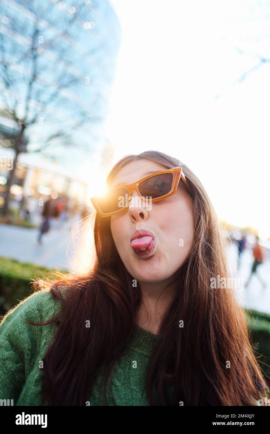 Junge Frau mit Sonnenbrille, die vor dem hellen, klaren Himmel aus der Zunge ragt Stockfoto
