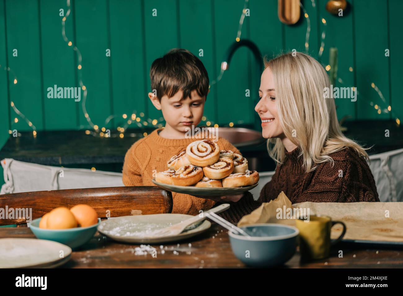 Lächelnde Mutter, die dem Sohn zu Weihnachten gebackene Zimtbrötchen zeigt Stockfoto