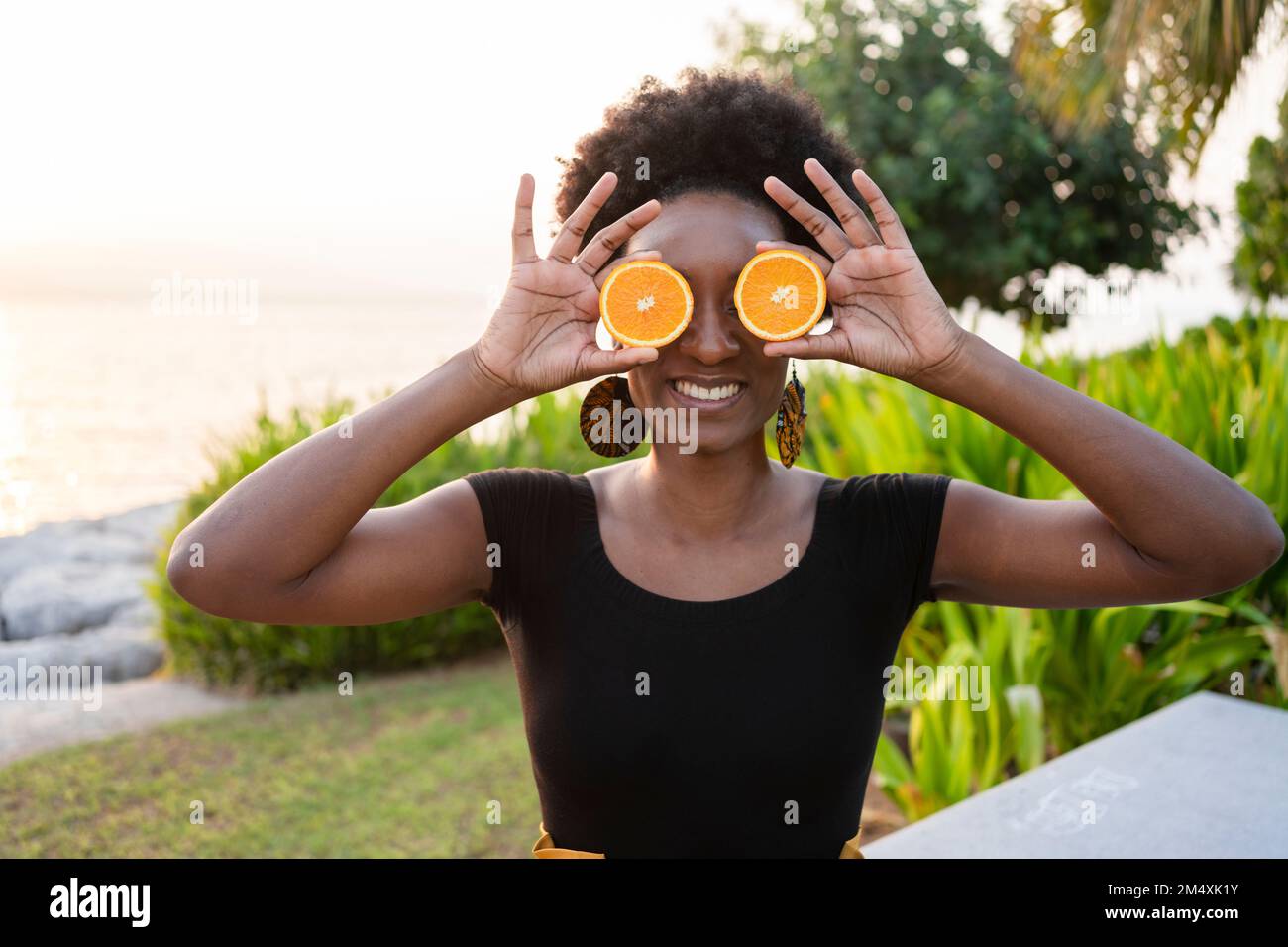 Glückliche Frau, die Orangenscheiben vor den Augen hält Stockfoto