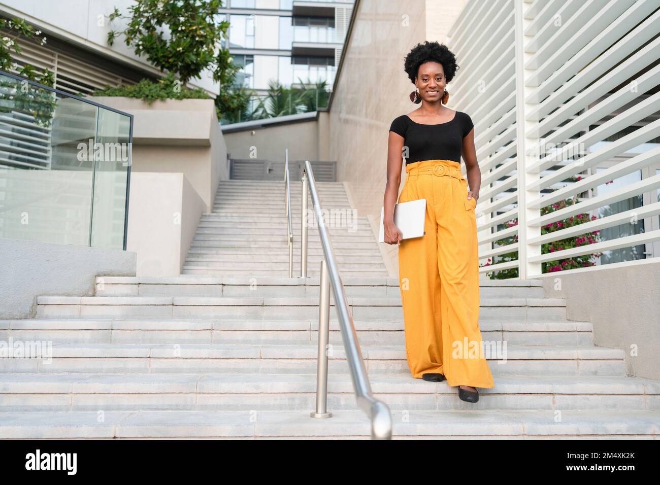 Lächelnde Frau mit Laptop, die die Treppe hinunterfährt Stockfoto