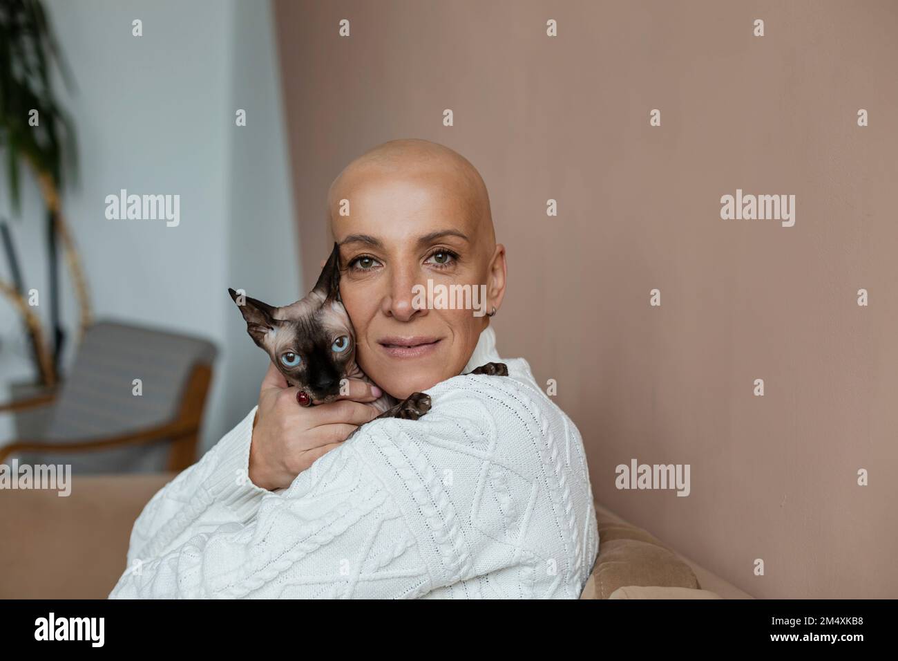 Reife, haarlose Frau, die die Sphynx-Katze auf dem Sofa umarmt Stockfoto