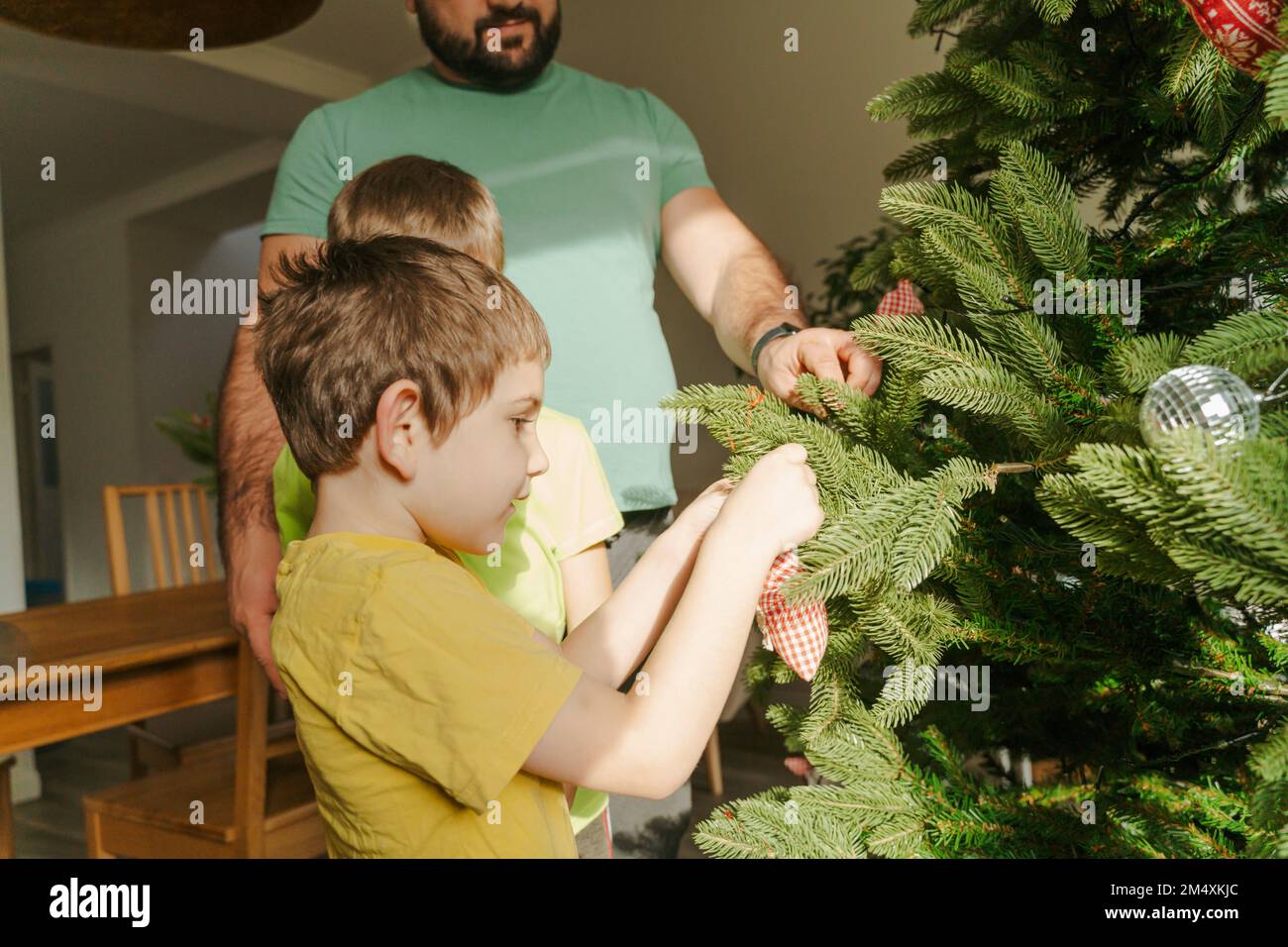Vater, der Söhnen hilft, den Weihnachtsbaum zu Hause zu schmücken Stockfoto