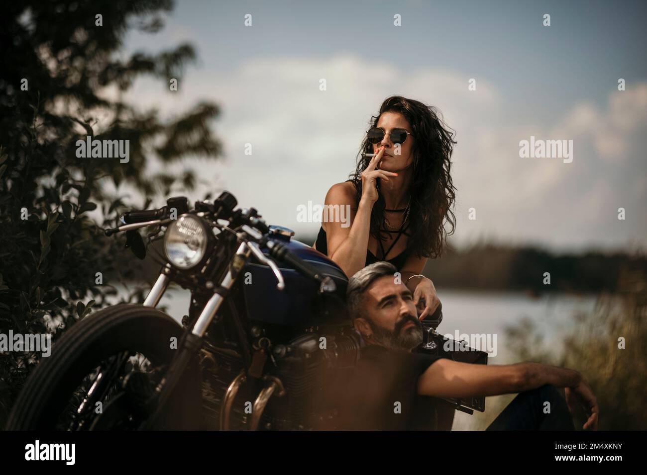 Reifer Mann mit einer Frau, die eine Zigarette raucht und sich auf dem Motorrad lehnt Stockfoto