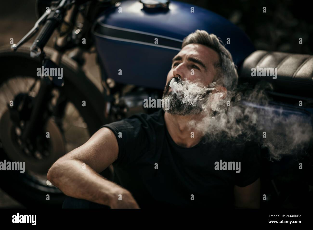 Ein Mann sitzt am Motorrad und raucht eine Zigarette Stockfoto