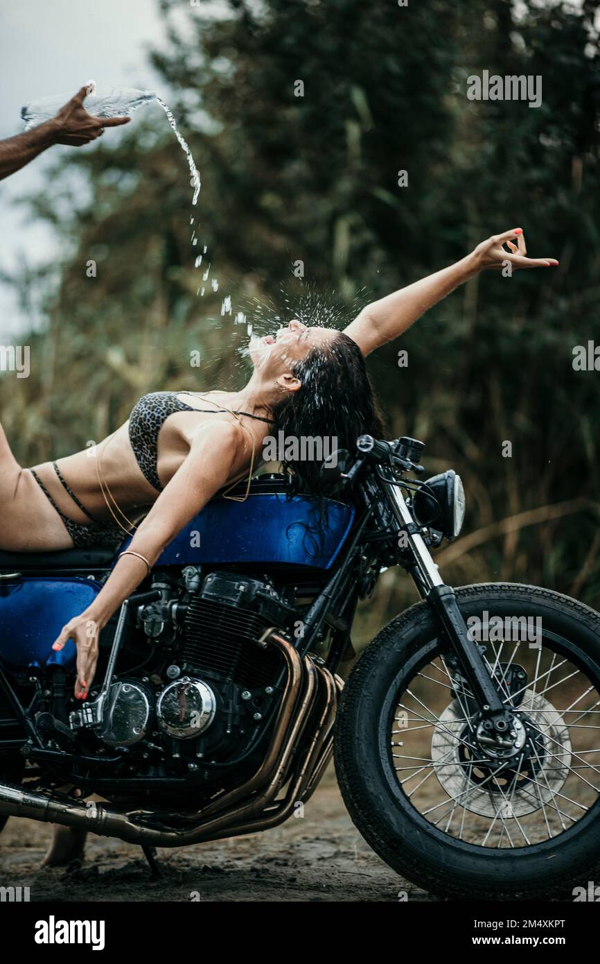 Reifer Mann, der Wasser in den Mund einer Frau gießt, die auf dem Motorrad liegt Stockfoto
