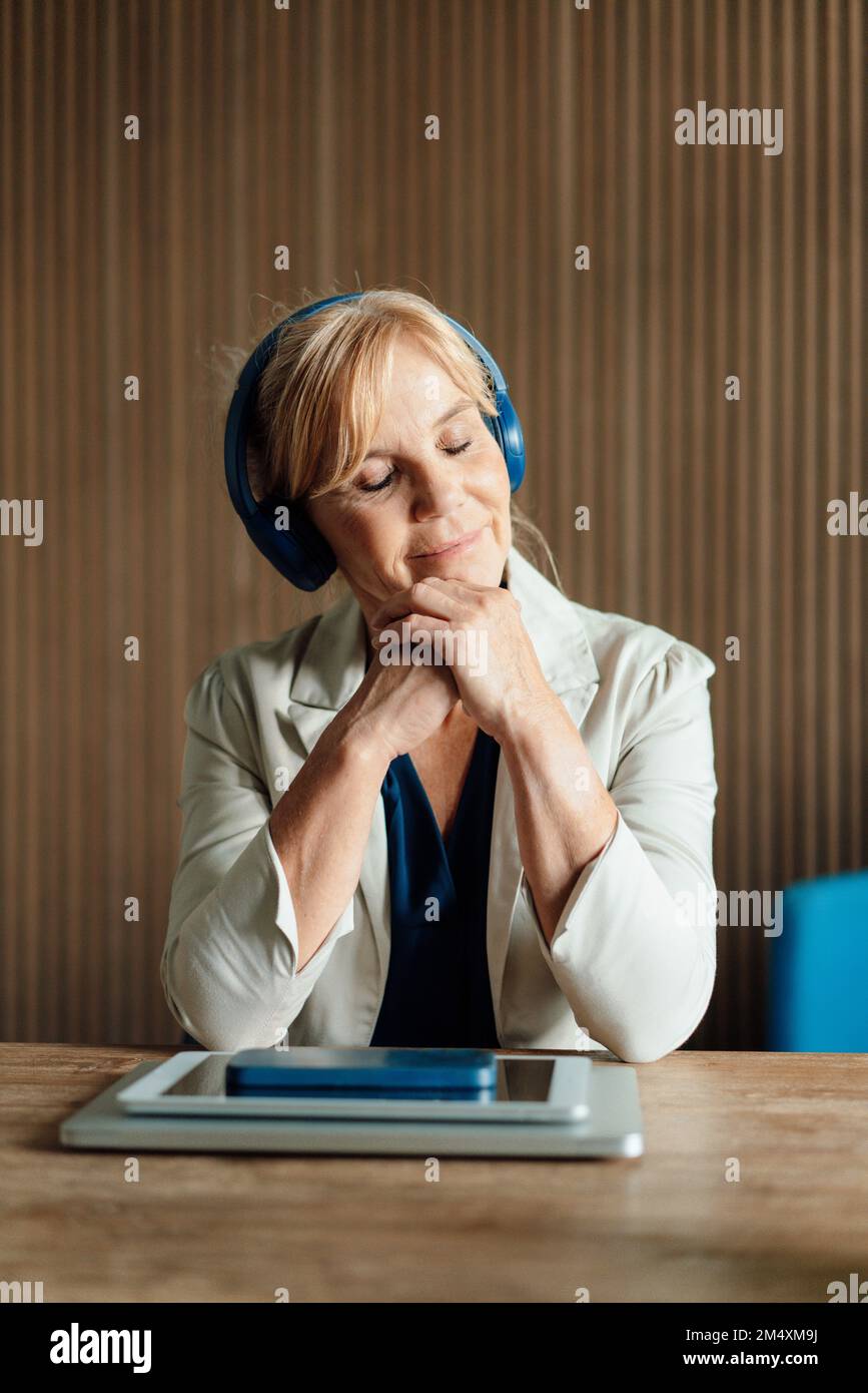 Geschäftsfrau, die Musik mit kabellosen Technologien auf dem Schreibtisch hört Stockfoto