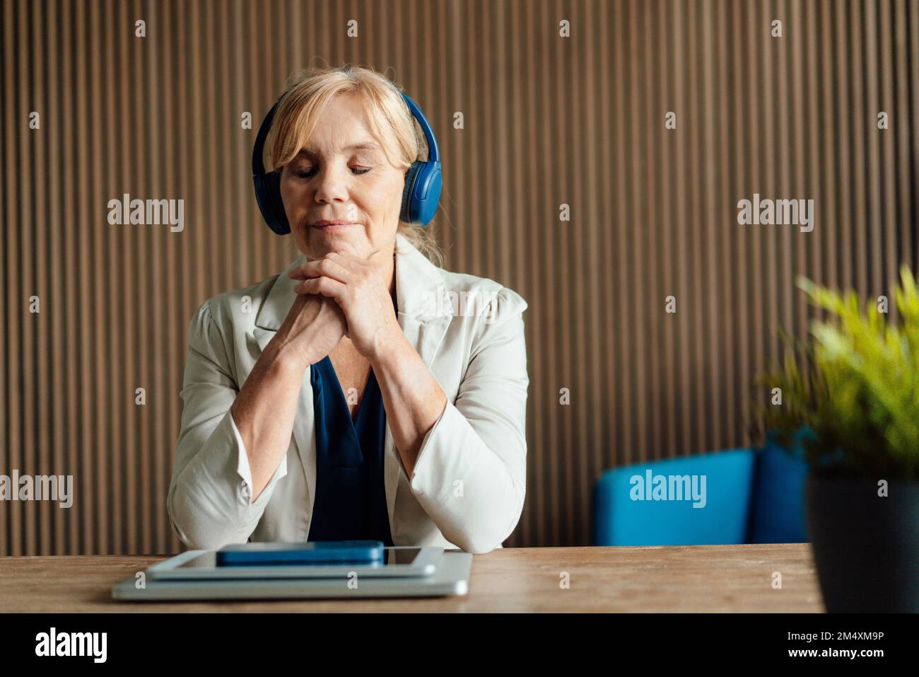Ältere Geschäftsfrau, die Musik mit kabellosen Technologien auf dem Schreibtisch hört Stockfoto