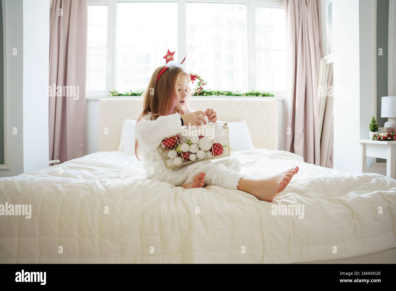 Ein Mädchen, das zu Hause mit einem Korb Weihnachtskugeln auf dem Bett sitzt Stockfoto