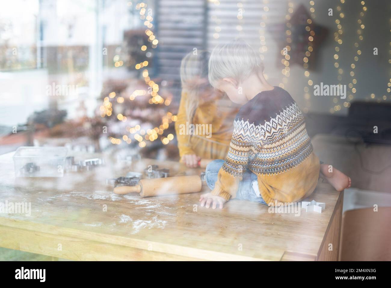 Geschwister, die Kekse auf dem Tisch zubereiten, durch Glas zu Hause gesehen Stockfoto