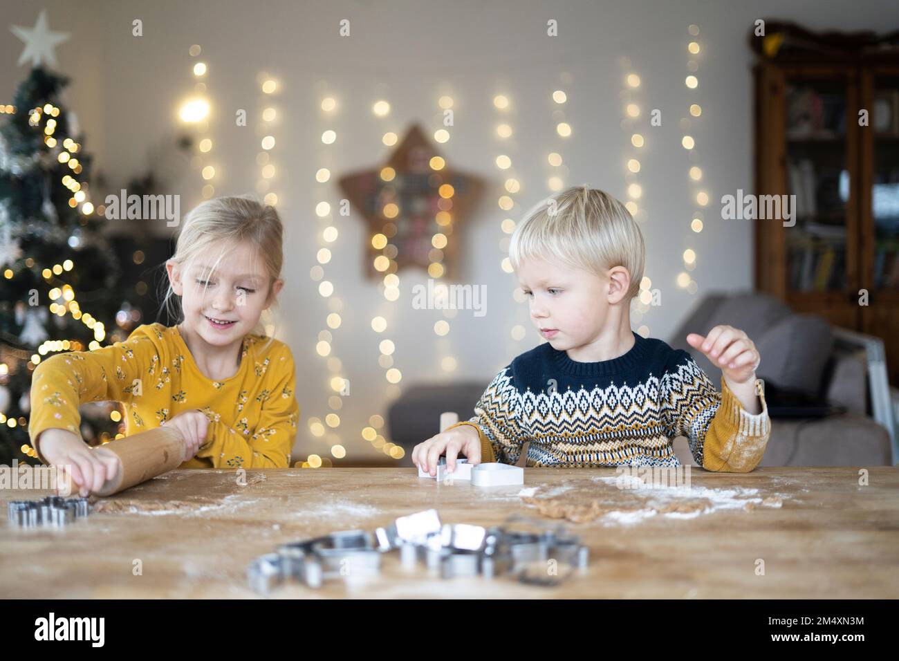 Lächelndes Mädchen, das zu Hause Teig von Bruder rollt Stockfoto