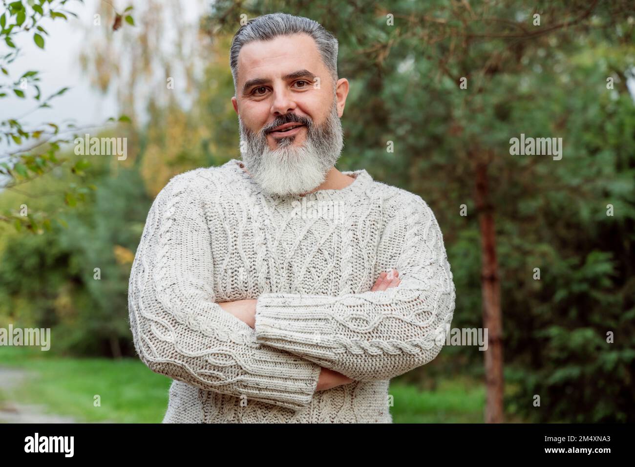 Ein erwachsener Mann, der einen Pullover trägt und mit gekreuzten Armen steht Stockfoto