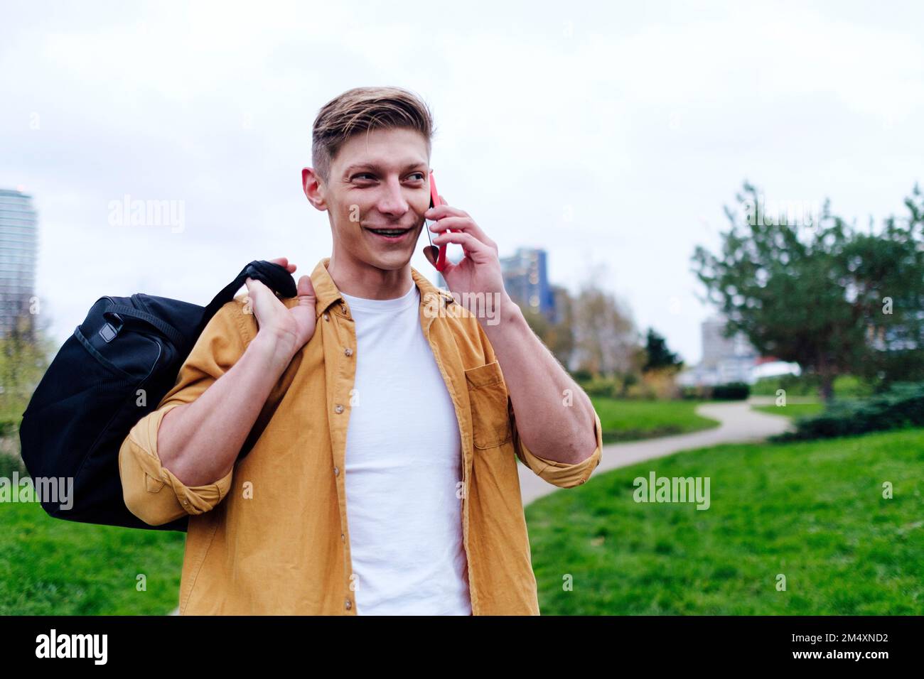 Ein junger Mann, der im Park in einer Smartphone-Tragetasche spricht Stockfoto